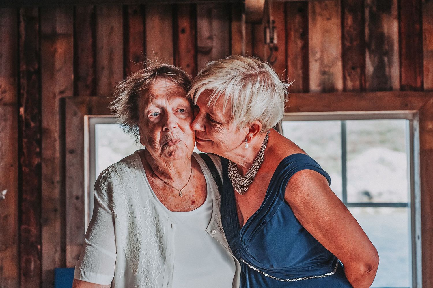 Two people sharing an intimate emotional moment in front of a rustic wooden wall with a window.