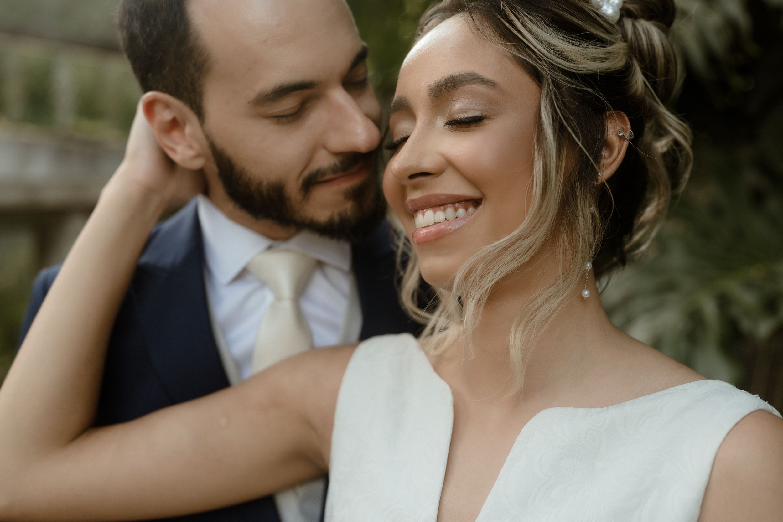 Romantic wedding couple embraces in front of tropical garden setting.