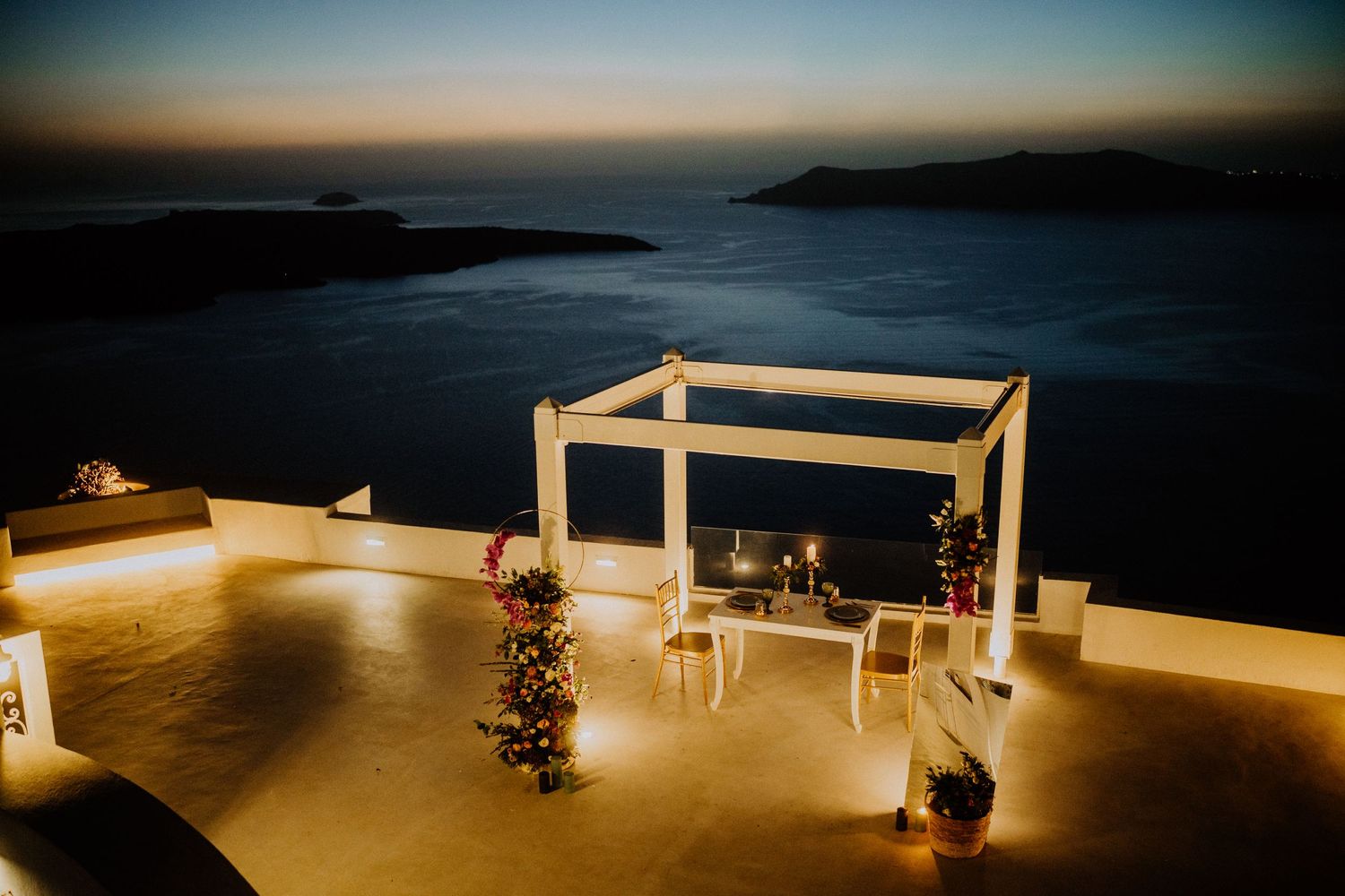 Romantic white canopy setup for evening dining with ocean view and twinkling lights at sunset.