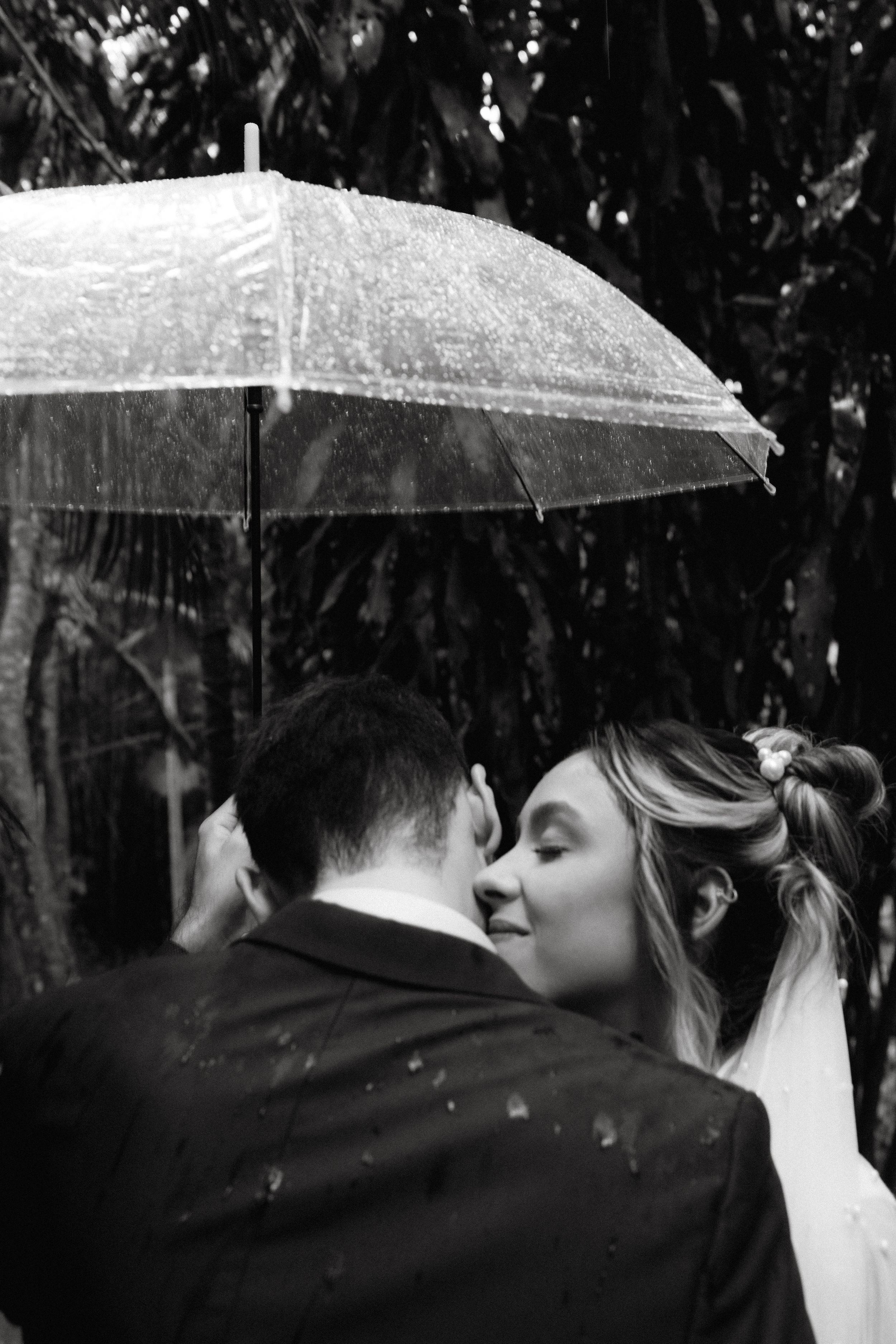 A black and white series of four photos showing a couple sharing a romantic moment under white umbrellas in the rain.
