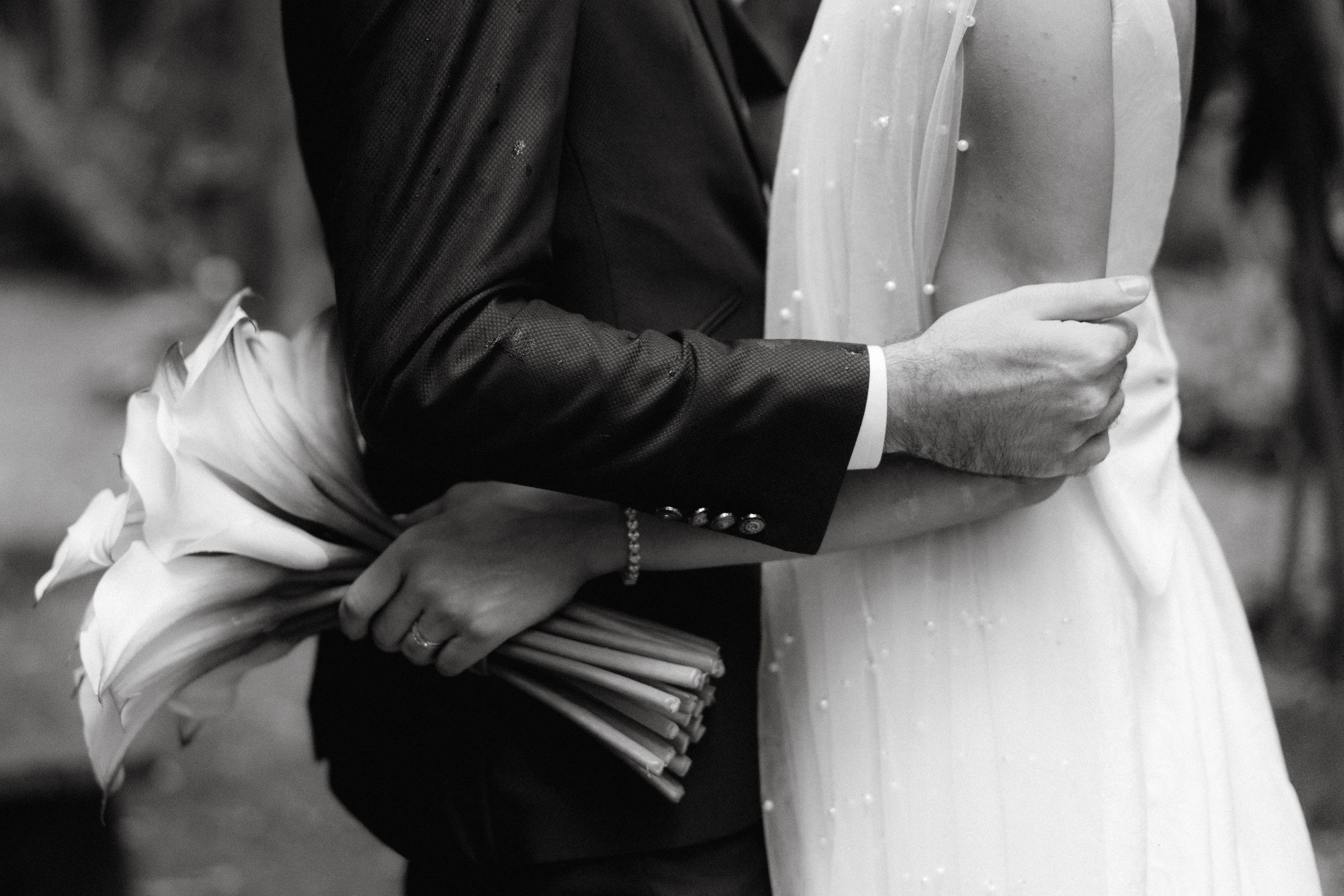 A black and white close-up of a couple embracing at a wedding, showing formal attire and a bridal bouquet.