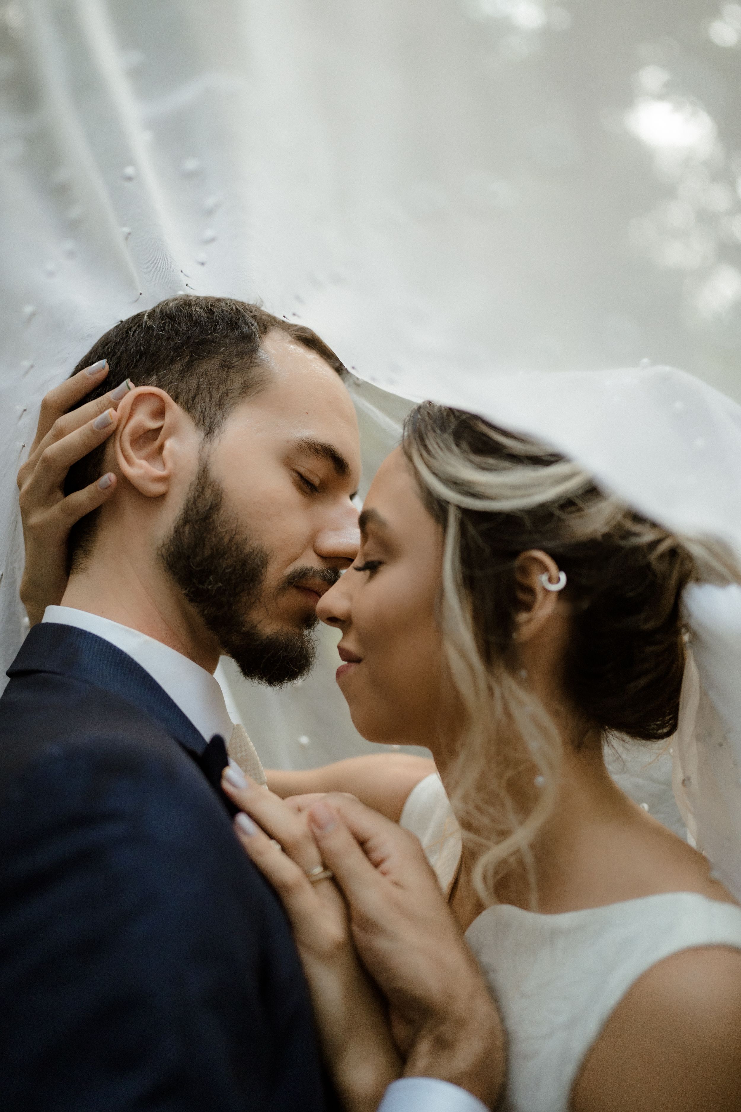 A romantic wedding couple shares an intimate moment under a veil as they tenderly embrace.
