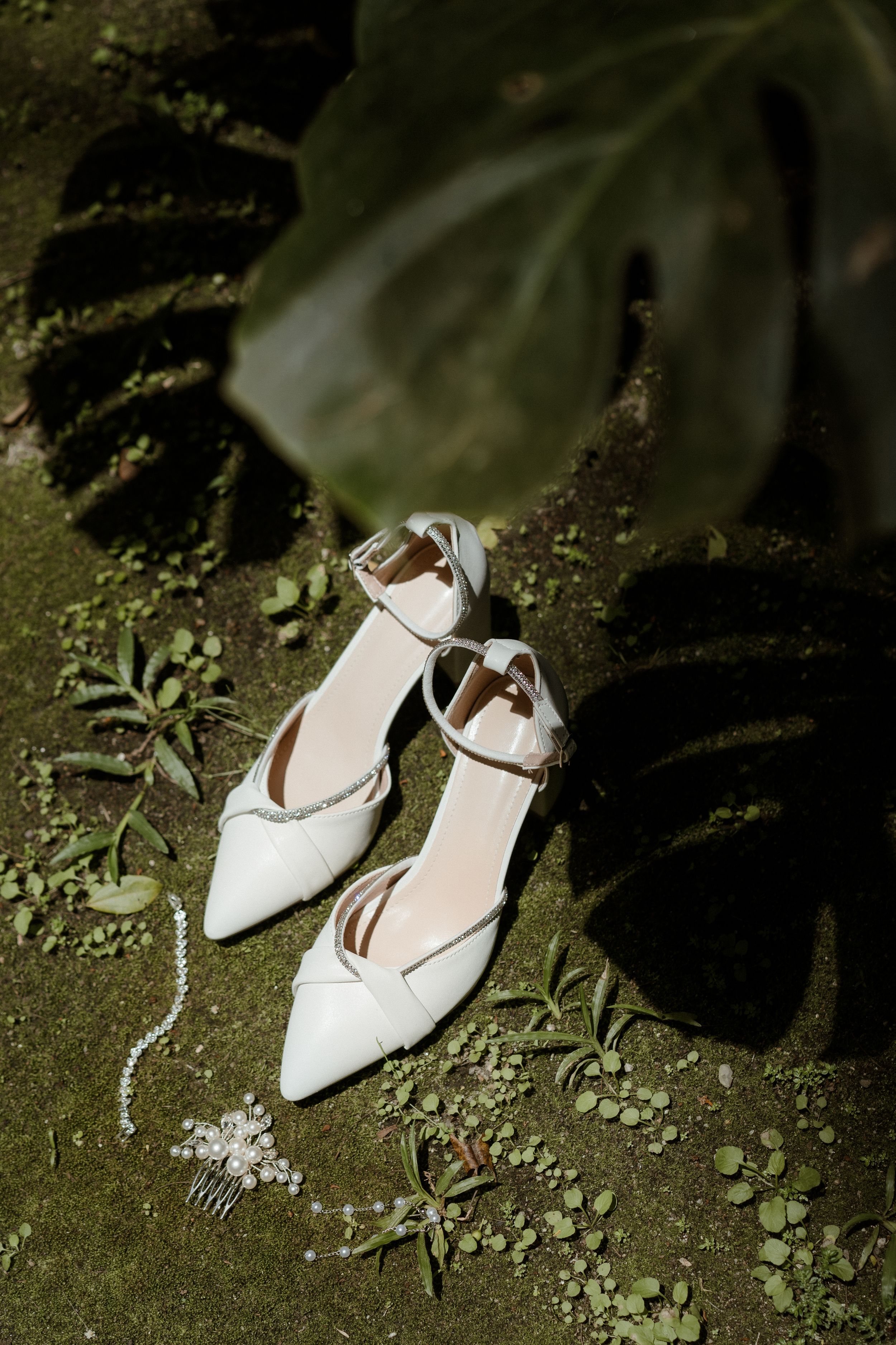 Elegant white bridal shoes placed on mossy ground in a garden setting.