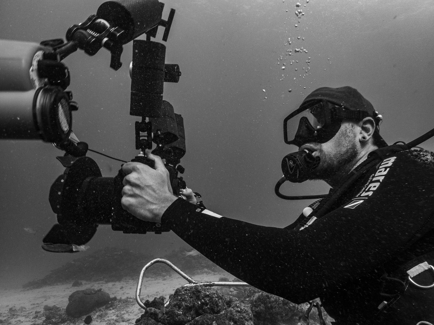 Black and white image of underwater photographer with camera gear in diving gear.