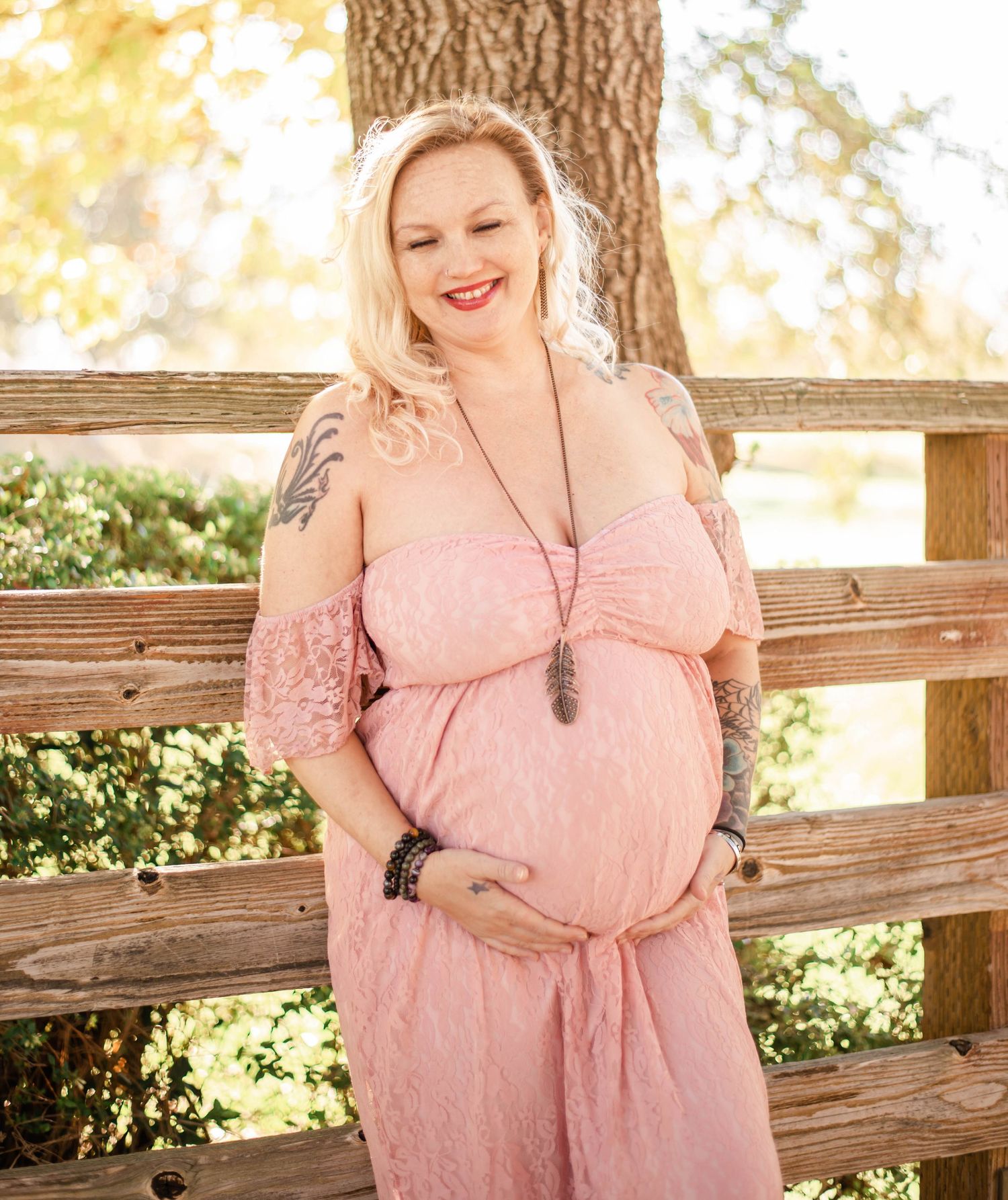 Outdoor maternity portraits featuring pink lace dress and rustic wooden fence with natural lighting.