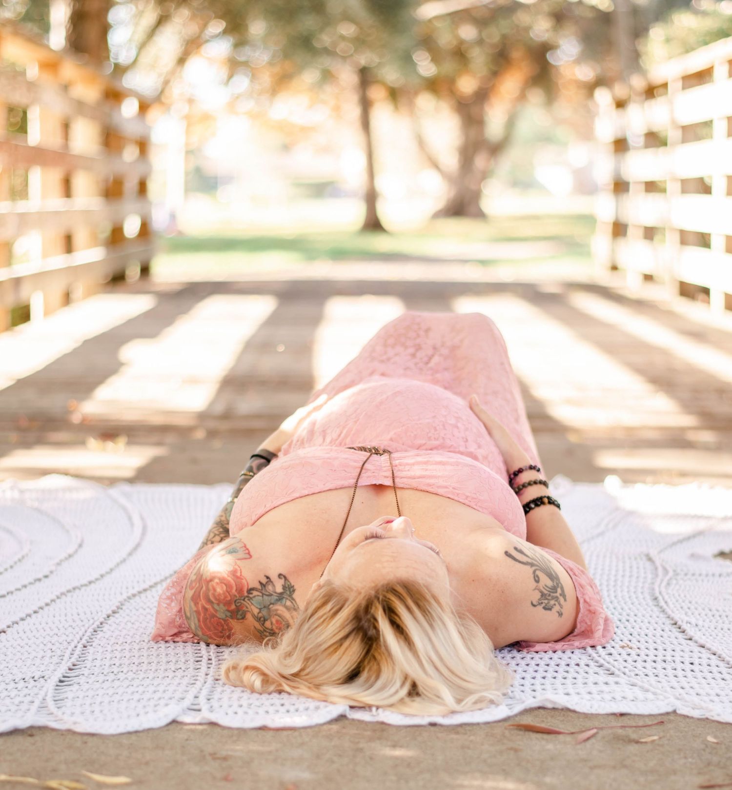 Ethereal maternity photography with expecting mother laying on vintage lace blanket outdoors.