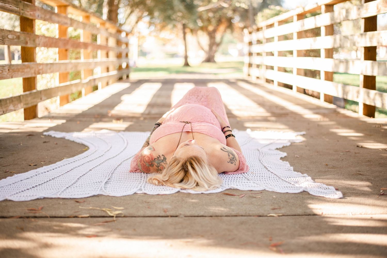 Outdoor maternity session with dappled sunlight and rustic wooden fence backdrop.
