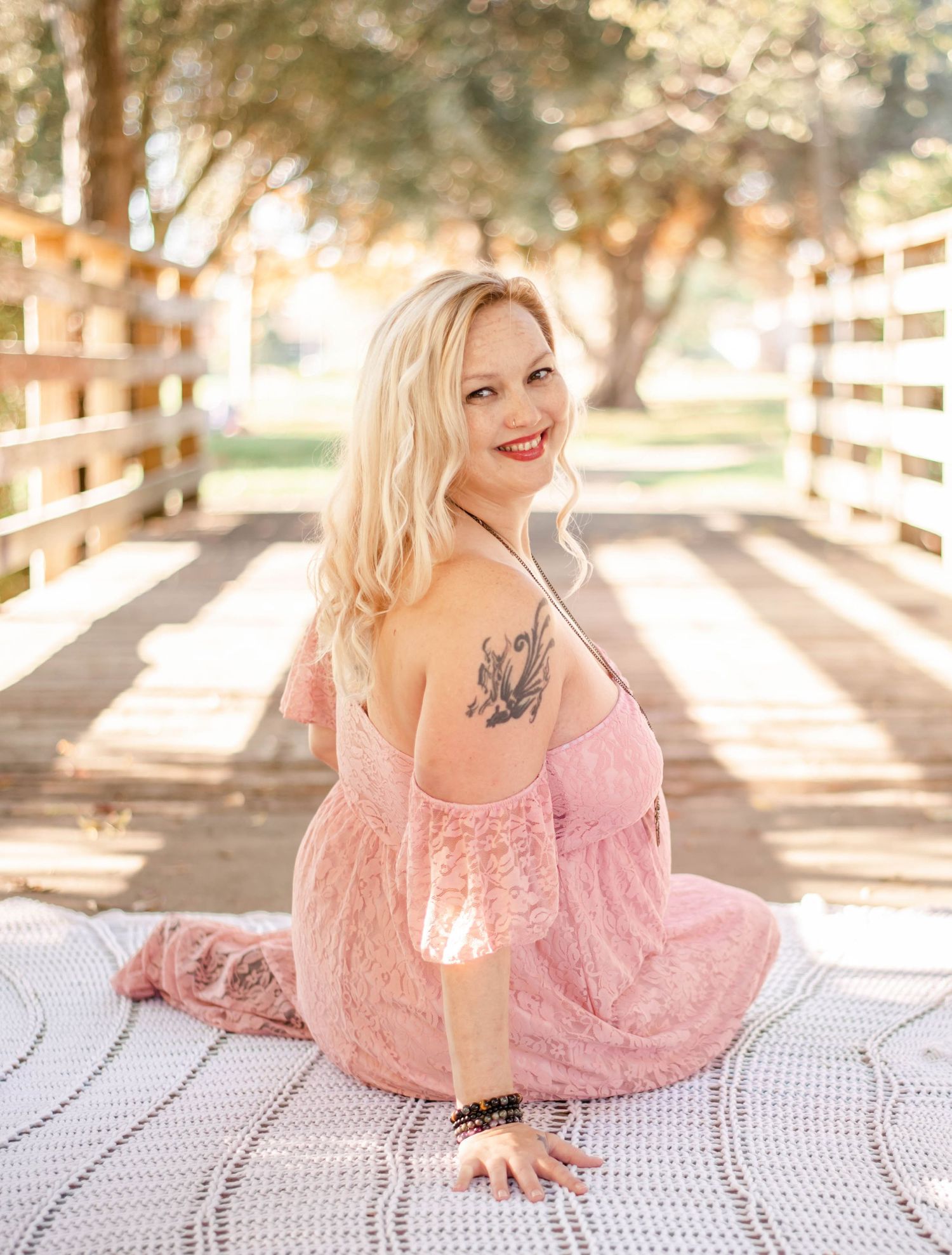 Artistic maternity portraits on white lace blanket with pink dress in natural outdoor setting.