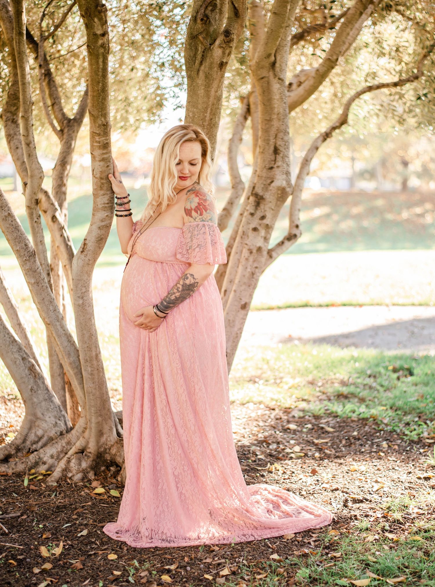 Enchanting maternity portraits beneath tree canopy featuring flowing pink lace dress.