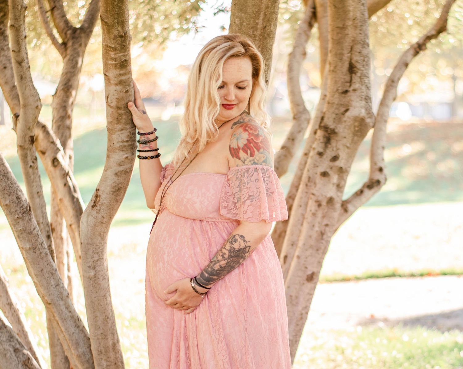 Dreamy maternity photography among trees with soft natural lighting and pink lace gown.