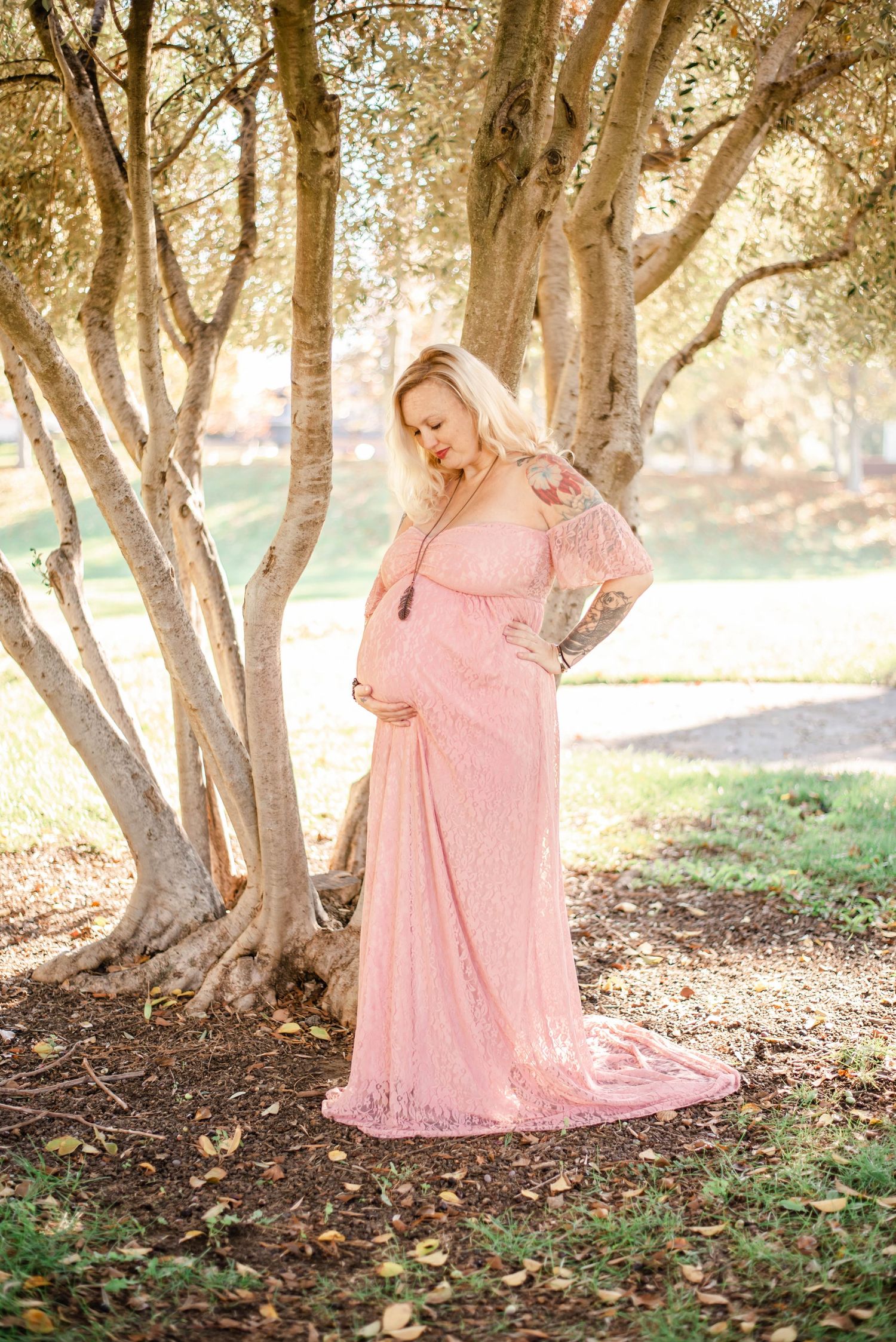 Natural light filters through trees during an outdoor maternity session featuring a pink dress.