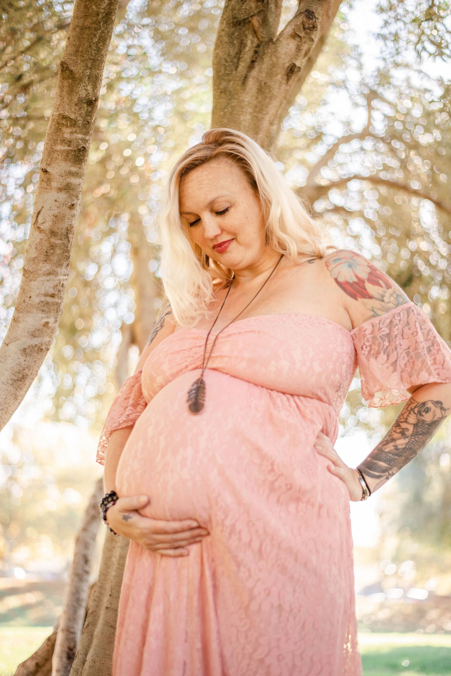 Dreamy maternity photos captured under trees showing a pink lace gown.