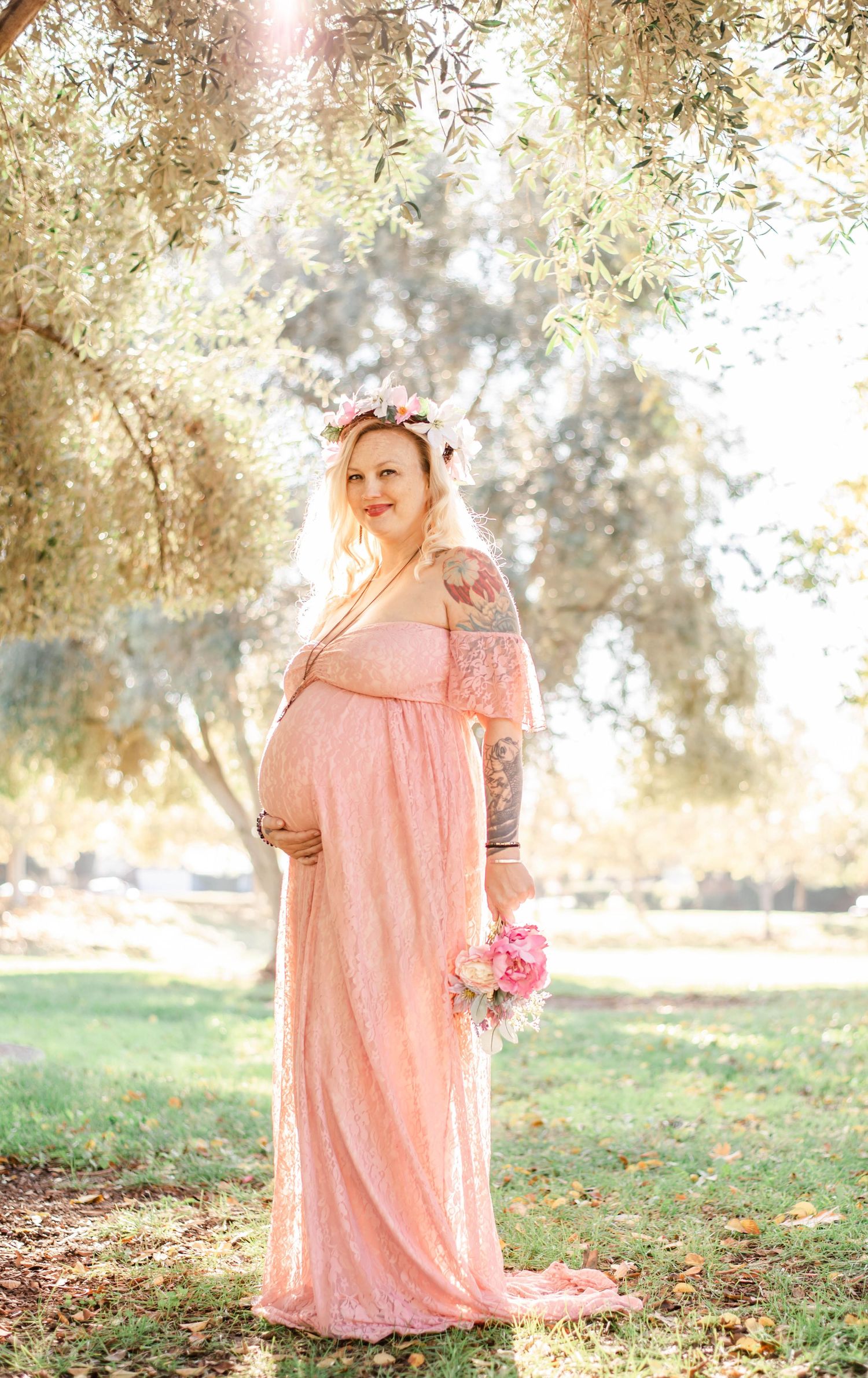 Romantic maternity photography session under trees with a pink flowing dress.