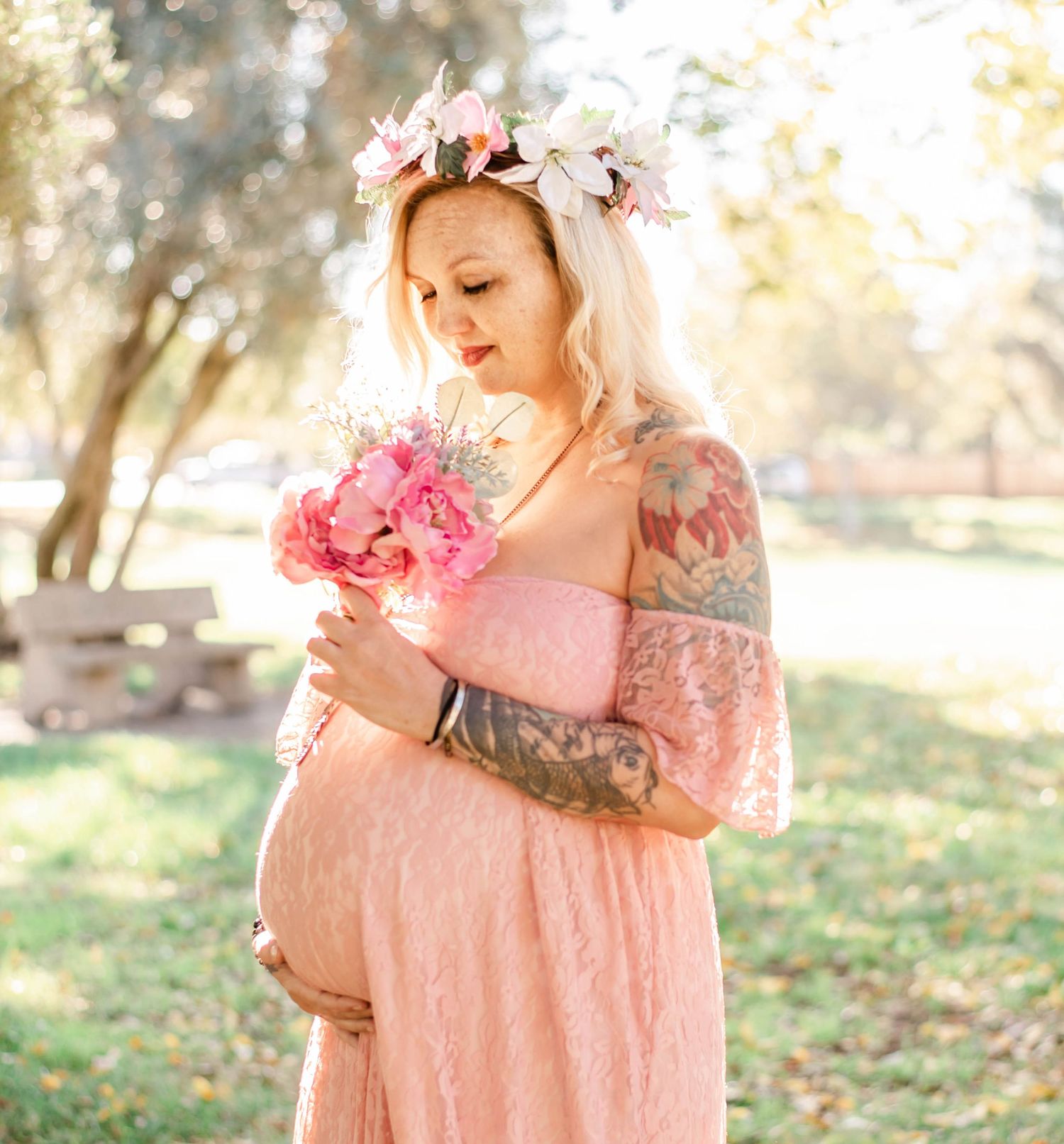 Maternity session featuring pink flowers and a lace dress in natural outdoor lighting.