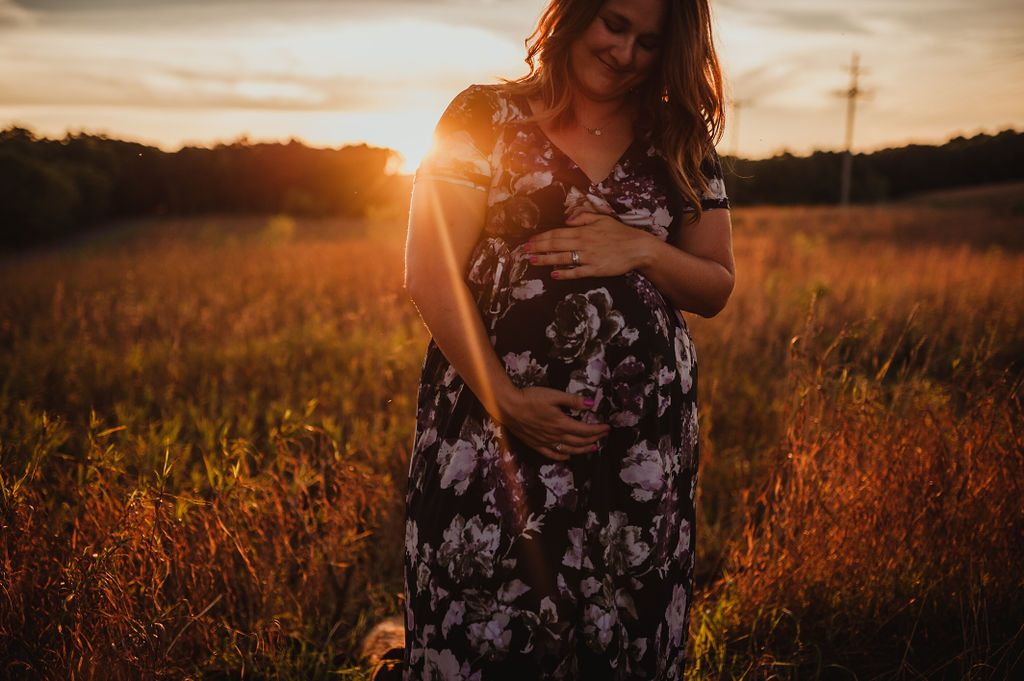 A floral maternity dress glows in warm sunset light across a meadow.