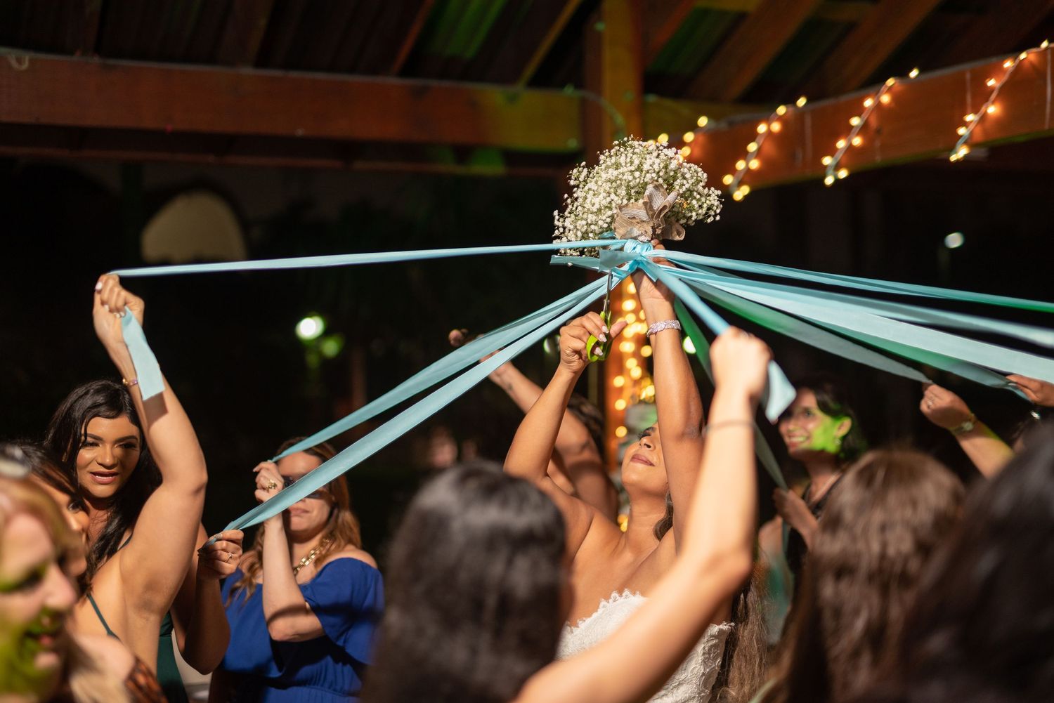 A group of guests reaches up to grab ribbons during a festive wedding reception celebration.