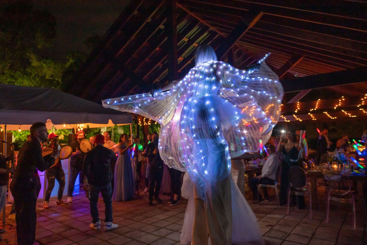 Illuminated LED dancers perform at a nighttime wedding reception under string lights.