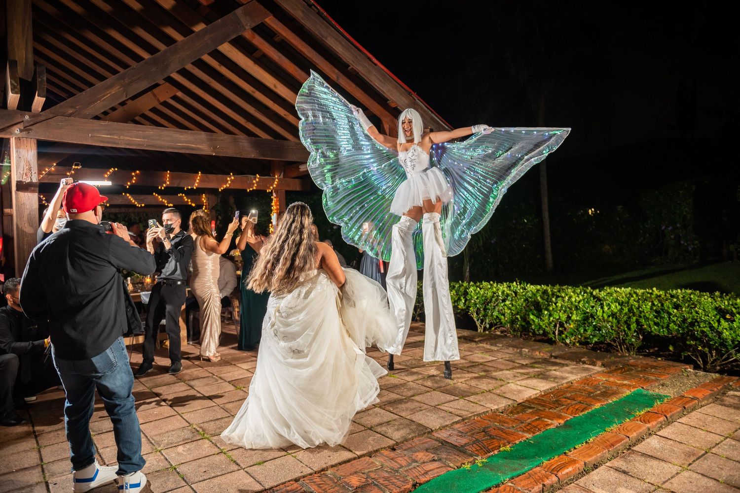 Performers in glowing winged costumes entertain guests at an outdoor wedding reception.