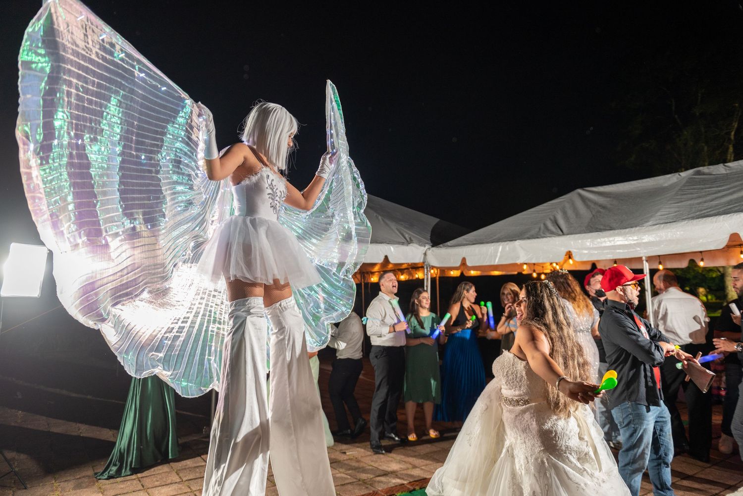 LED wing performers create a magical light show during an outdoor evening wedding celebration.