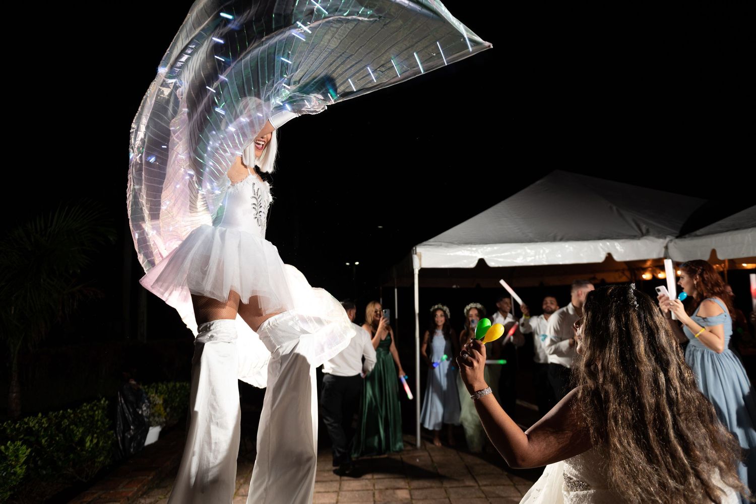 A performer in illuminated costume dances at night under a white tent during wedding festivities.