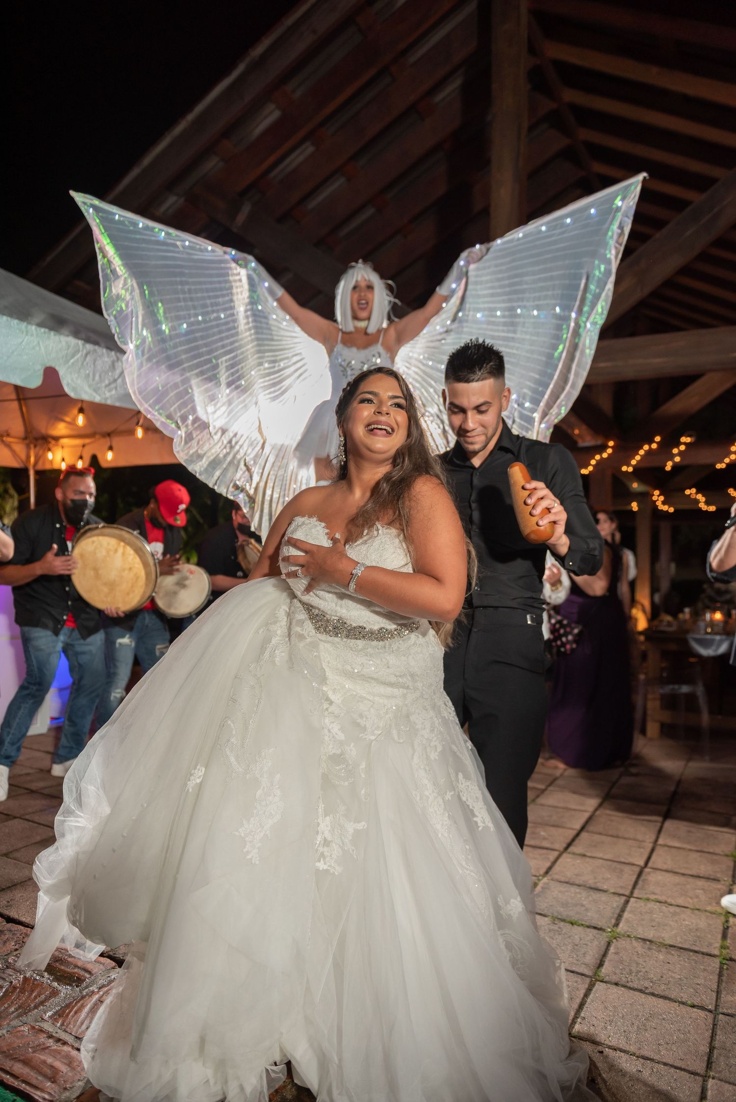 A joyful couple dances at their wedding reception, with the bride wearing iridescent fairy wings and a white gown.