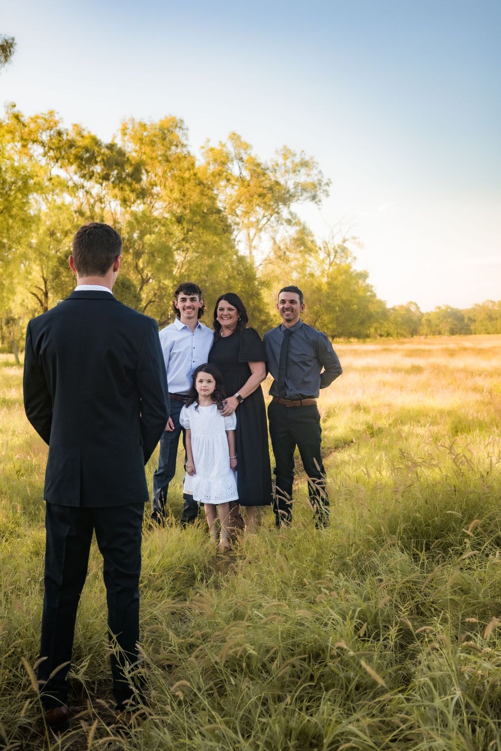 Family portrait session at sunset with group posing in tall grass field.