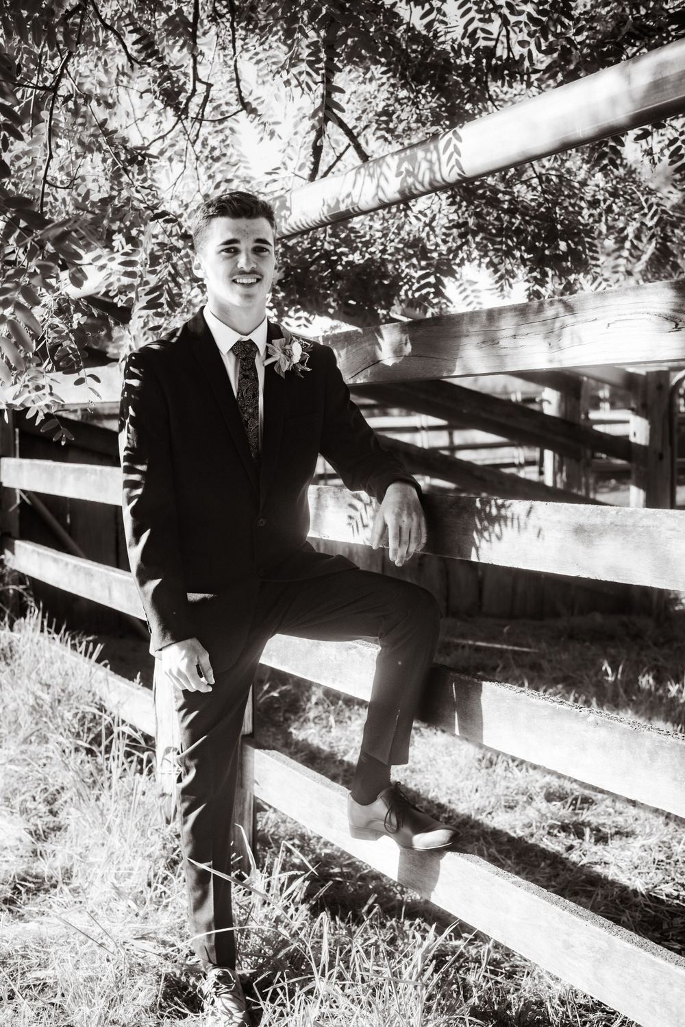 Formal portrait of person sitting on rustic wooden fence in black and white.