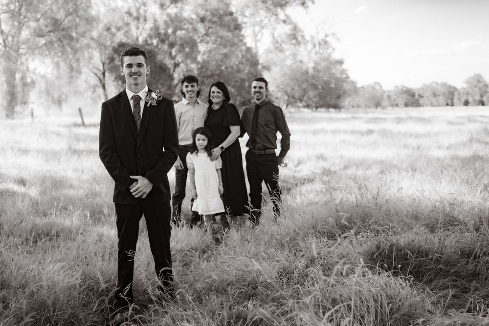 Group poses in black and white photo on rural path with trees in background.