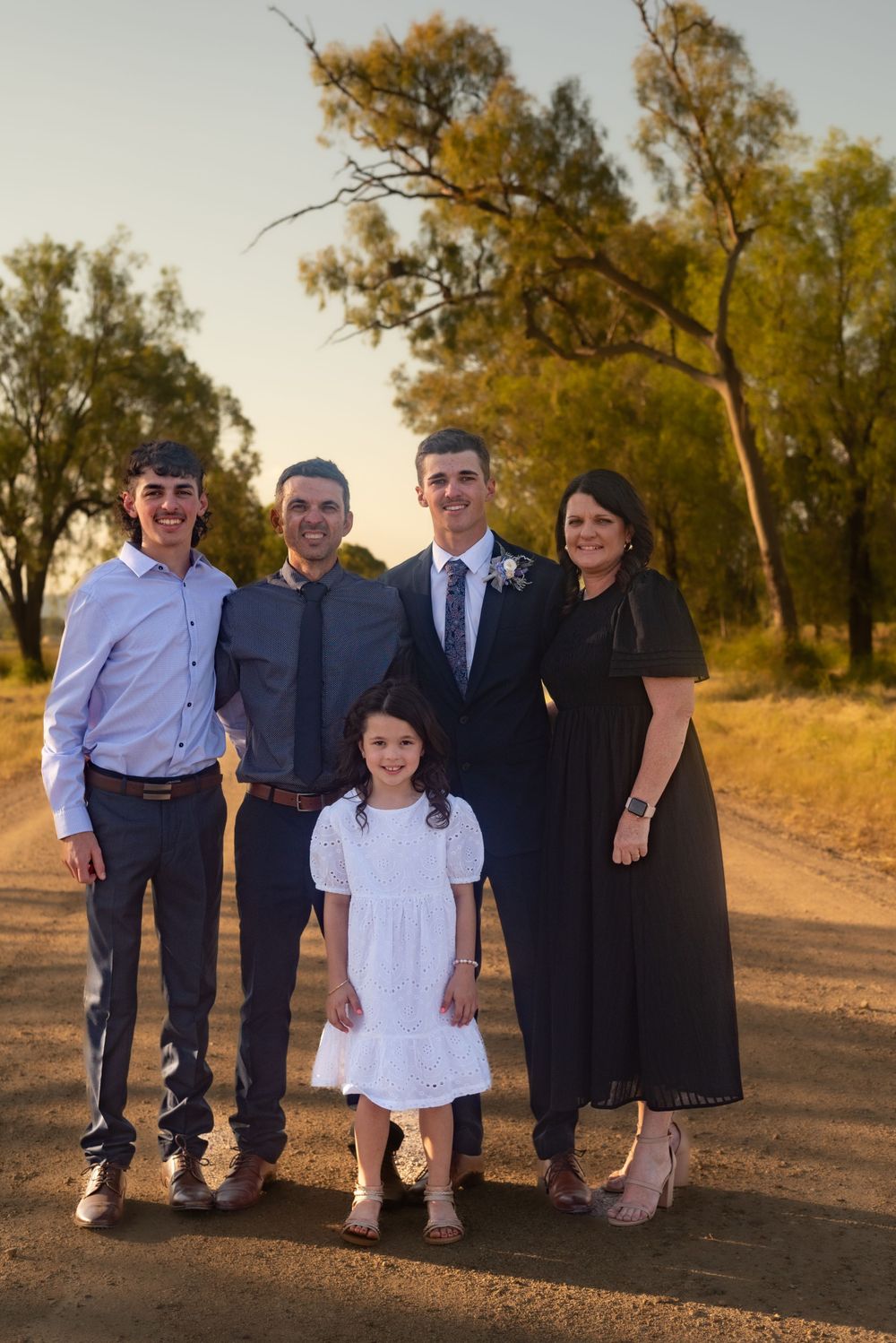 Family group portrait on dirt road with trees during golden hour.