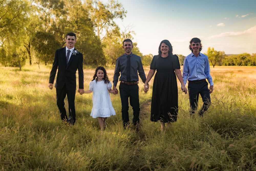 Family of five holding hands while standing in golden field at sunset.