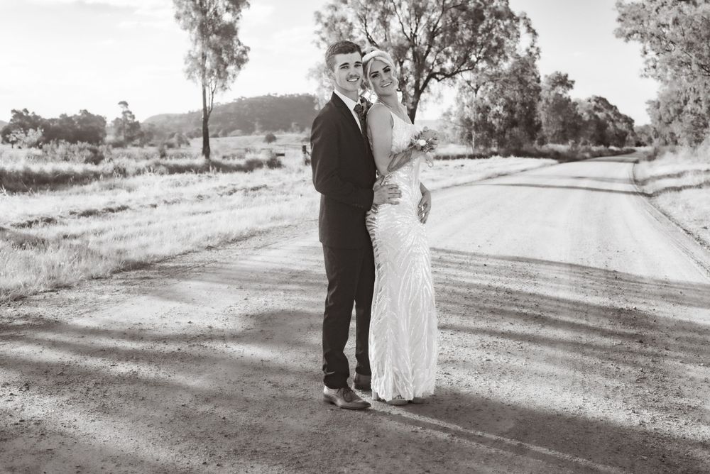 A black and white wedding photo of a couple standing on a country road.
