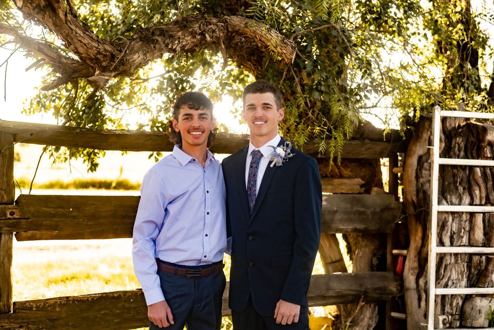 Two people posing by rustic wooden fence during golden hour.