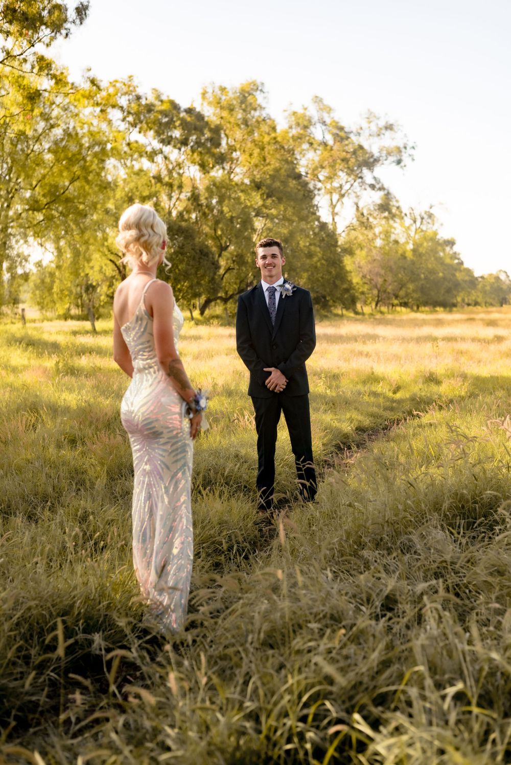 Wedding couple poses on a rustic dirt path during golden hour with trees and tall grass in the background.