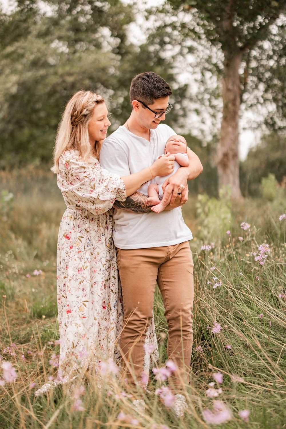 Couple cradles newborn among wildflowers in dreamy outdoor setting.