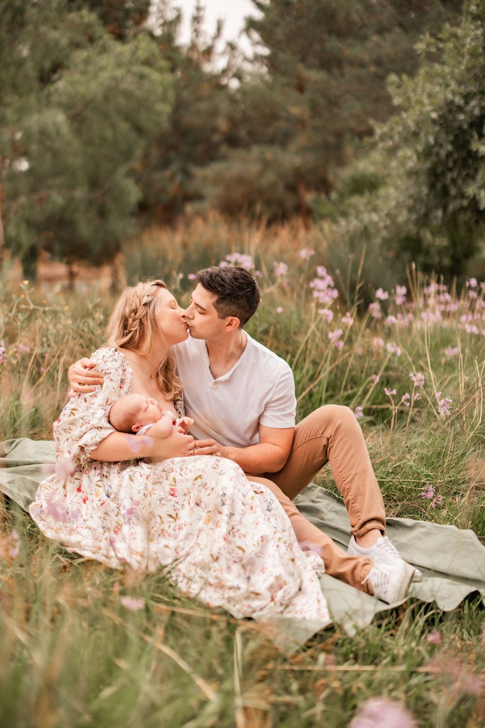 Loving family moment on a blanket surrounded by wildflowers and natural scenery.