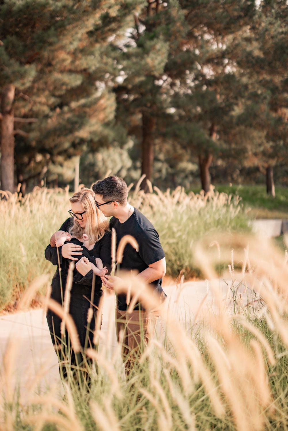 Romantic couple embracing among tall grass with sunlit forest in background.