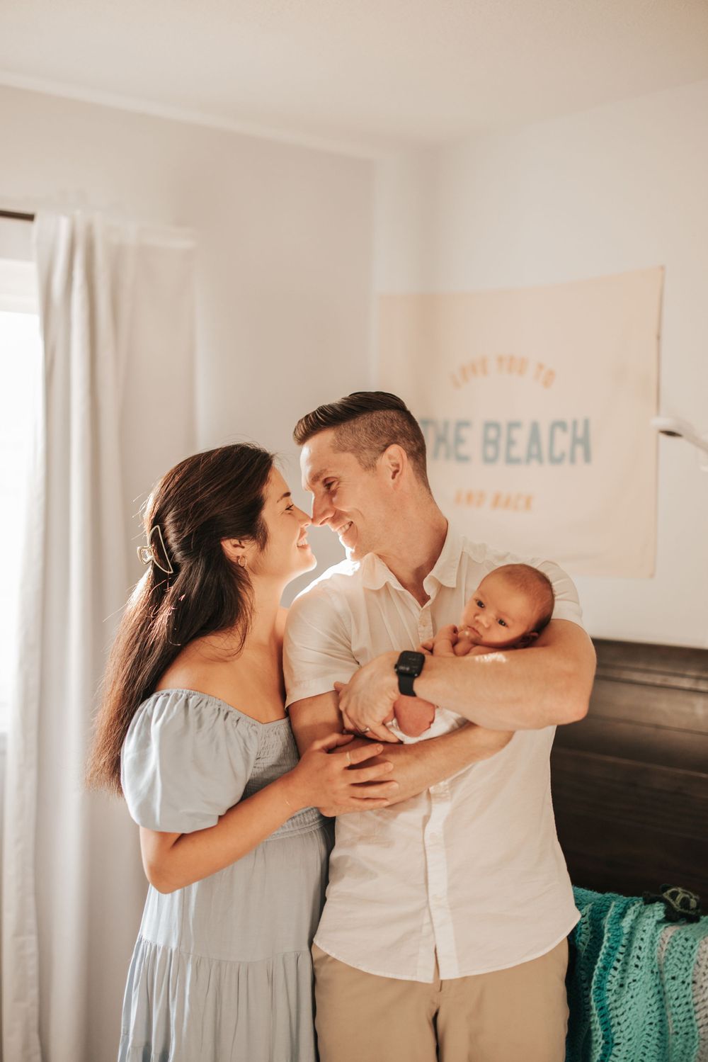 Intimate family moment in a bright room with a newborn baby and beachy wall art.