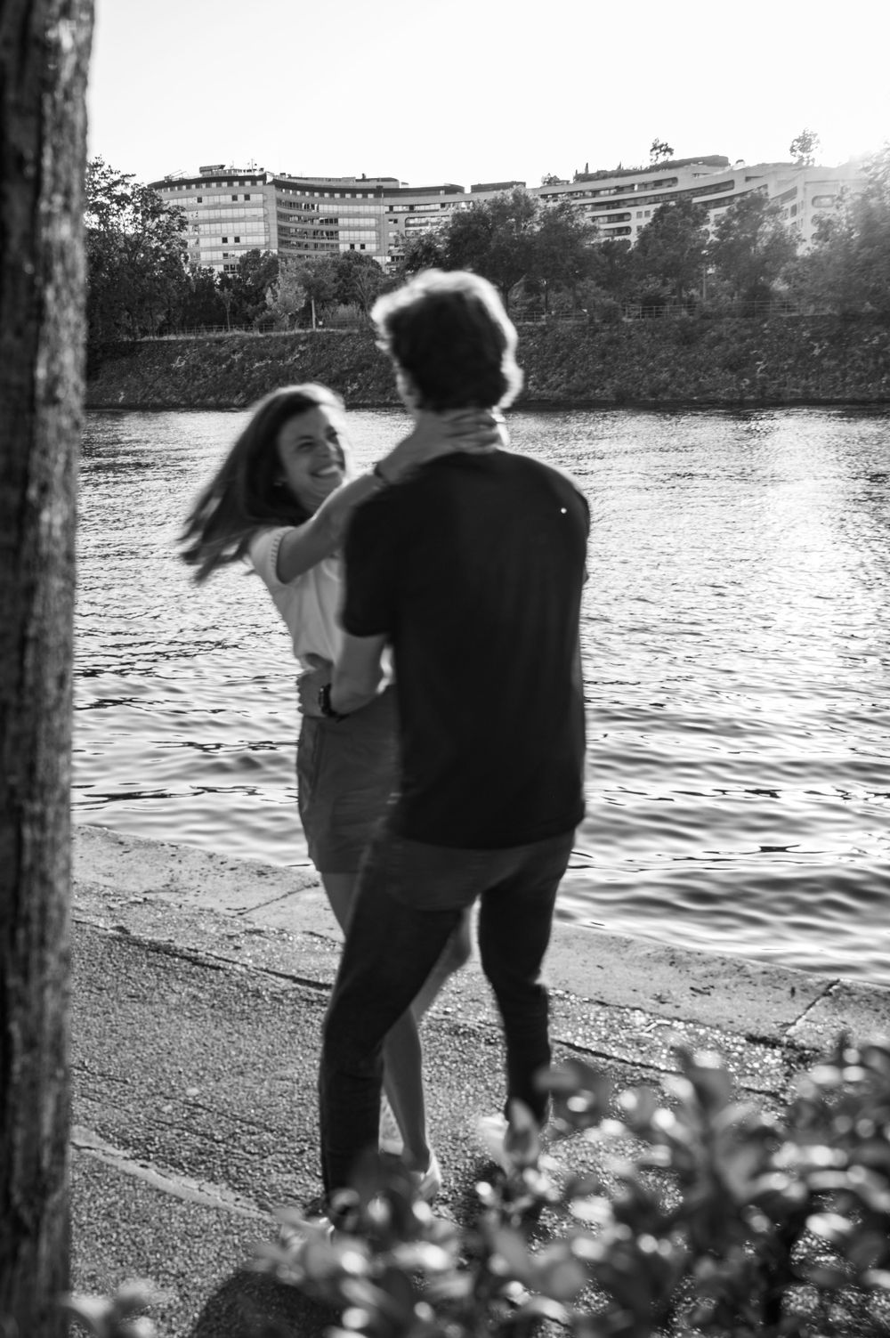 Black and white photo of a couple dancing playfully by the water.