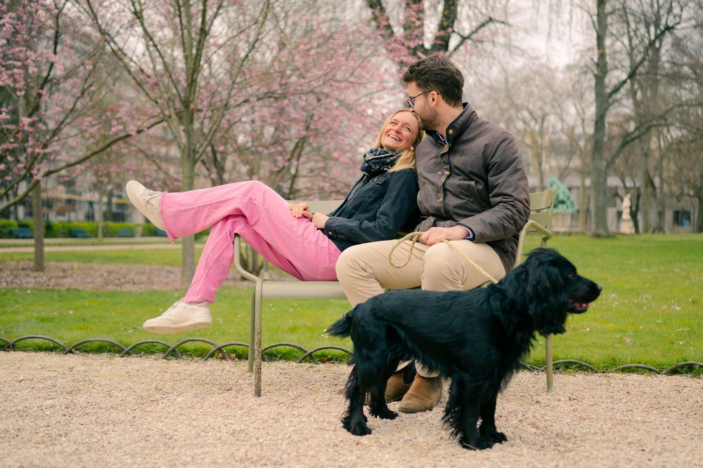 A couple relaxes on a bench with their black dog in a park during springtime.