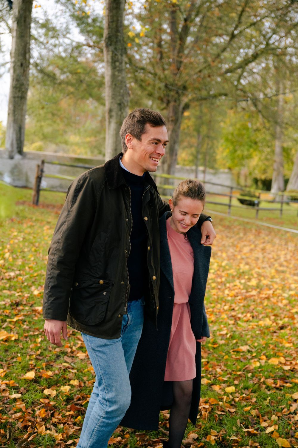 Two people walk together on fallen autumn leaves in a park setting during fall season.