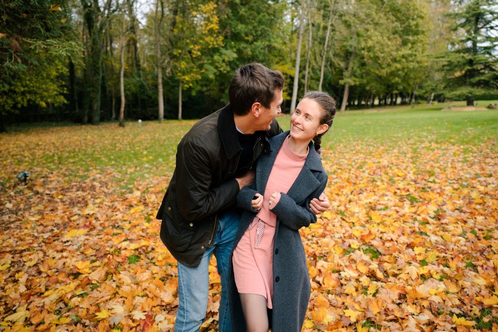 A couple shares a romantic moment in a park filled with vibrant autumn leaves during fall season.