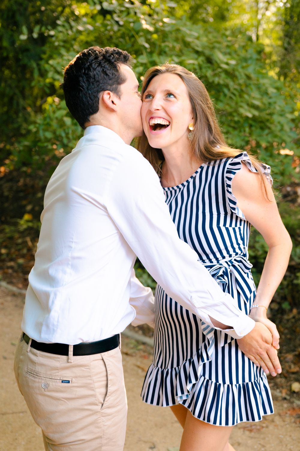 A couple in black and white striped dress and khaki pants share joyful dance moves in a sunlit outdoor setting.