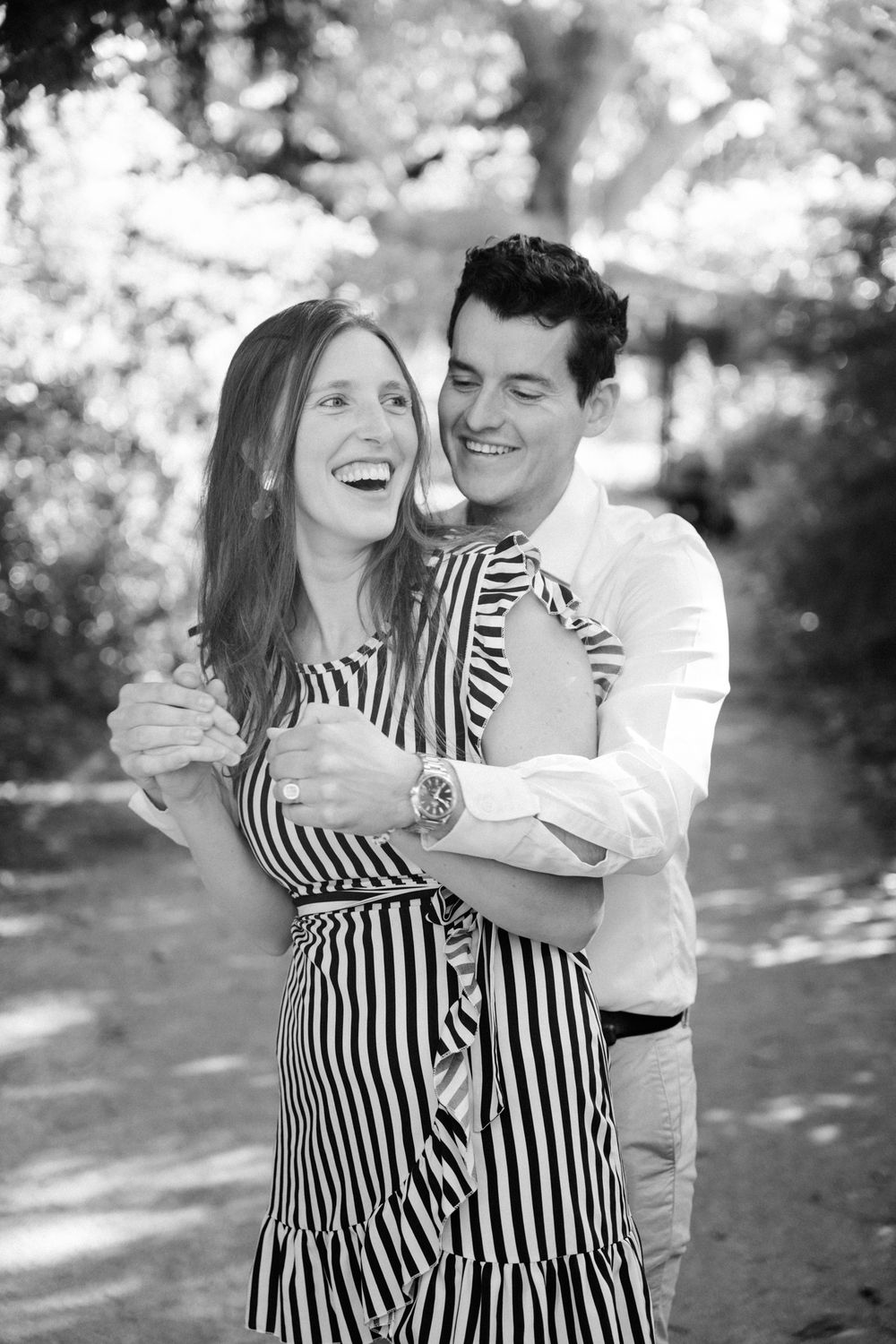 A couple shares a joyful embrace outdoors in a black and white photo series showing natural candid moments.