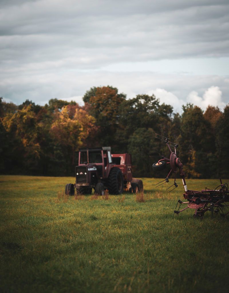 Red tractor sits in autumn field with farm equipment and trees in background.