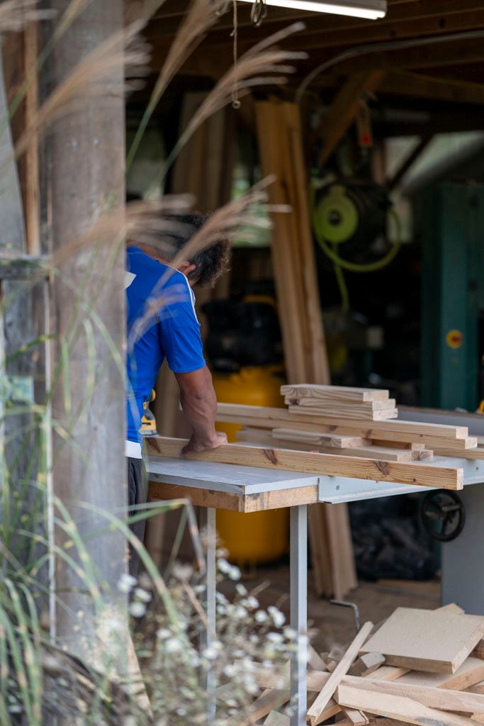 Woodworking workshop scene with lumber pieces on a workbench and blue-clad carpenter at work.