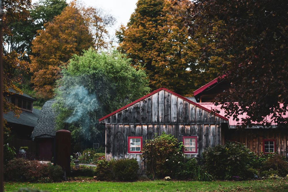 Rustic wooden barn with smoke rising from chimney surrounded by fall foliage.