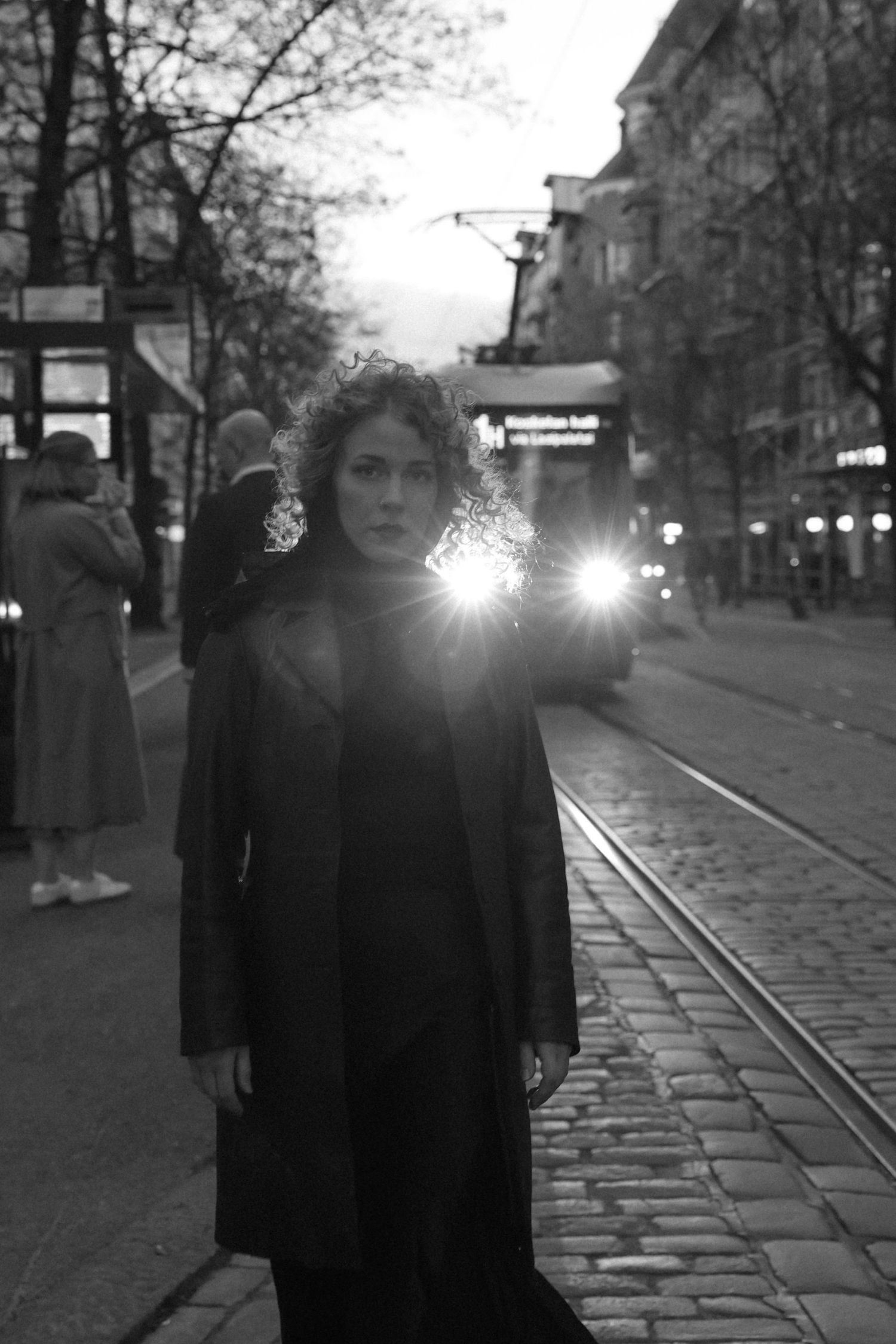 Black and white street scene with tram tracks and lights reflecting on a cobblestone street in an urban setting at dusk.