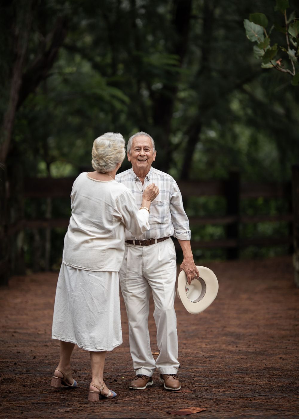 A tender moment between a couple in all white clothing on a wooded path.