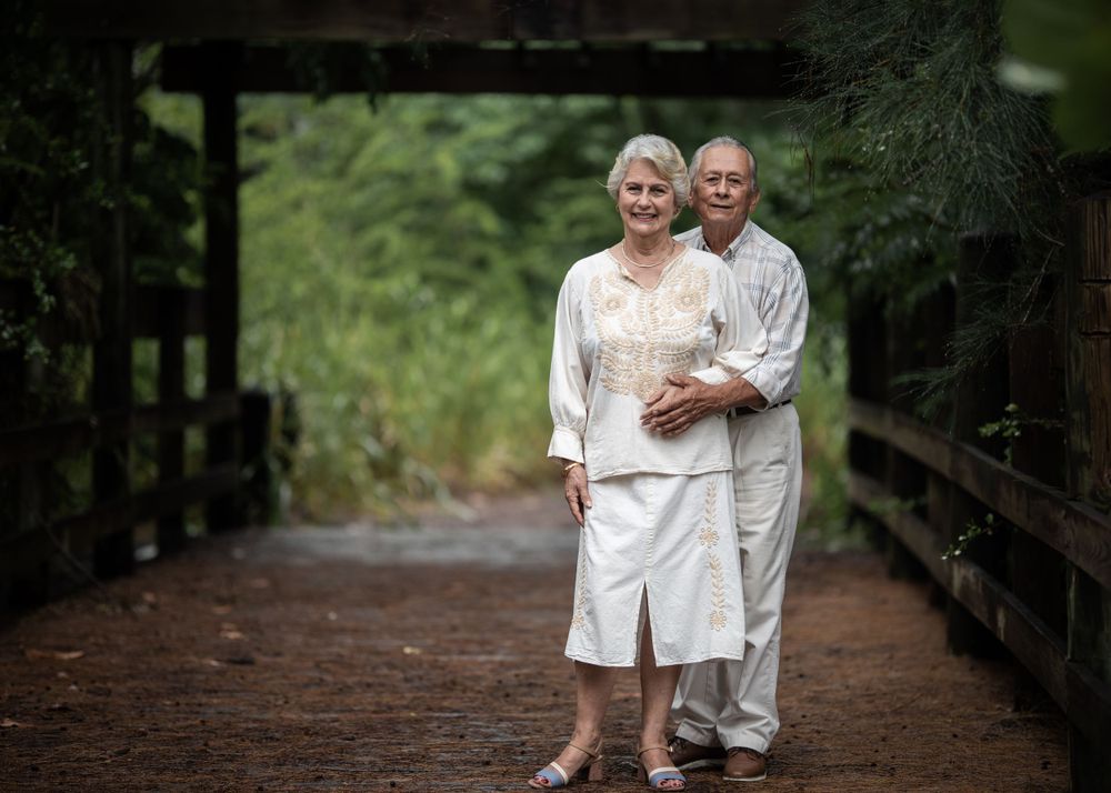 A couple poses together on a wooden bridge in a serene forest setting.