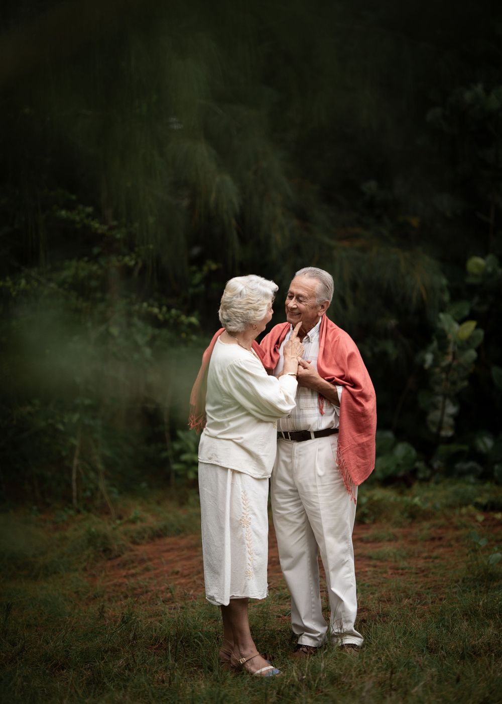A tender moment between an elderly couple as they dance together against a dark green background.